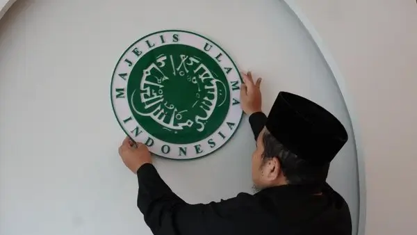 Fatwa MUI  Bitchology Seorang Muslim sedang menempelkan plang bertuliskan MUI di dinding menggambarkan simbol lembaga keagamaan yang berjarak dari semangat keterbukaan dan dialog